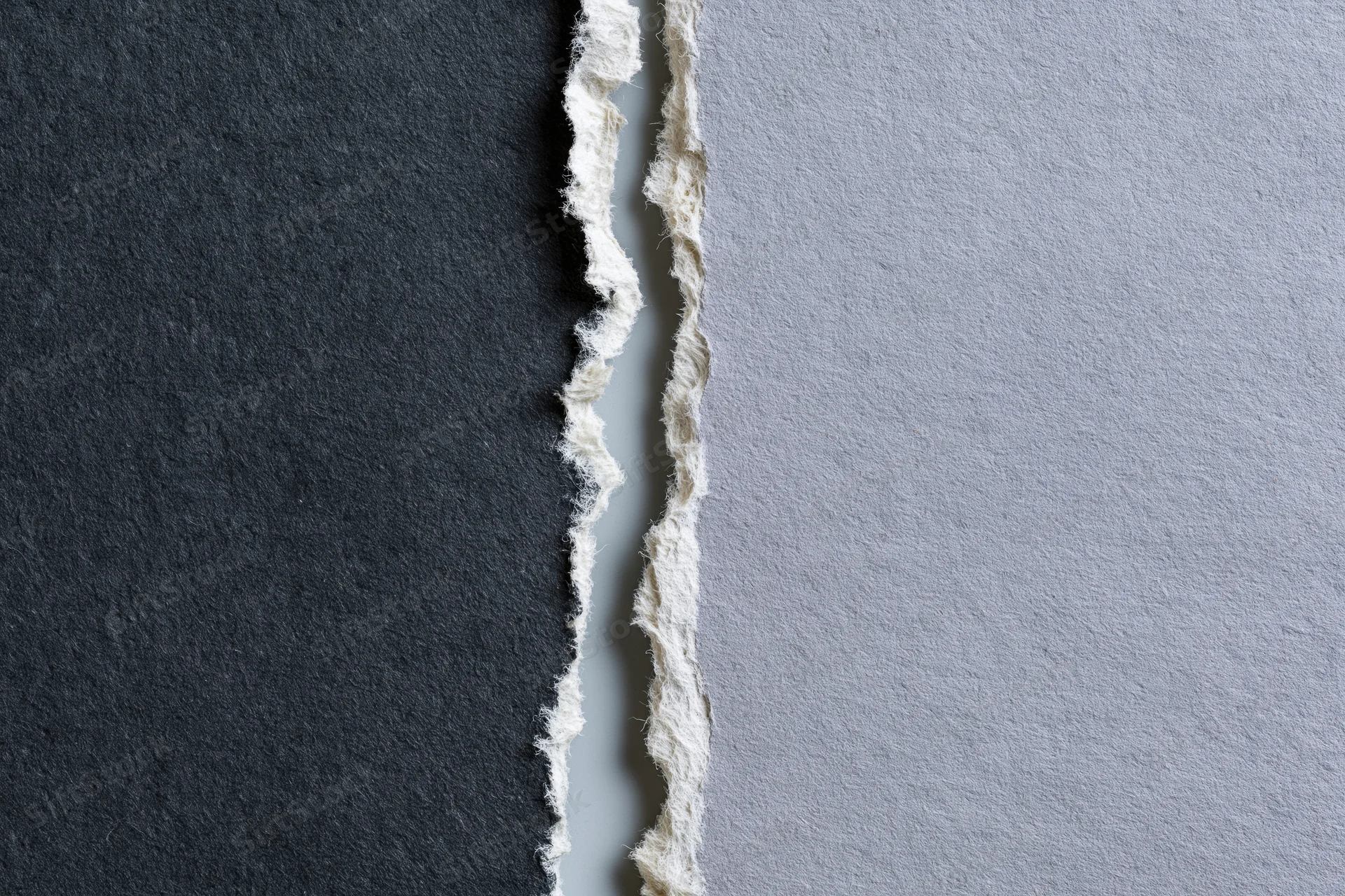 Two torn sheets of paper placed side by side with ragged edges and contrasting dark charcoal and light gray surfaces