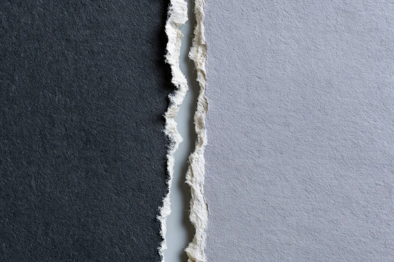 Two torn sheets of paper placed side by side with ragged edges and contrasting dark charcoal and light gray surfaces