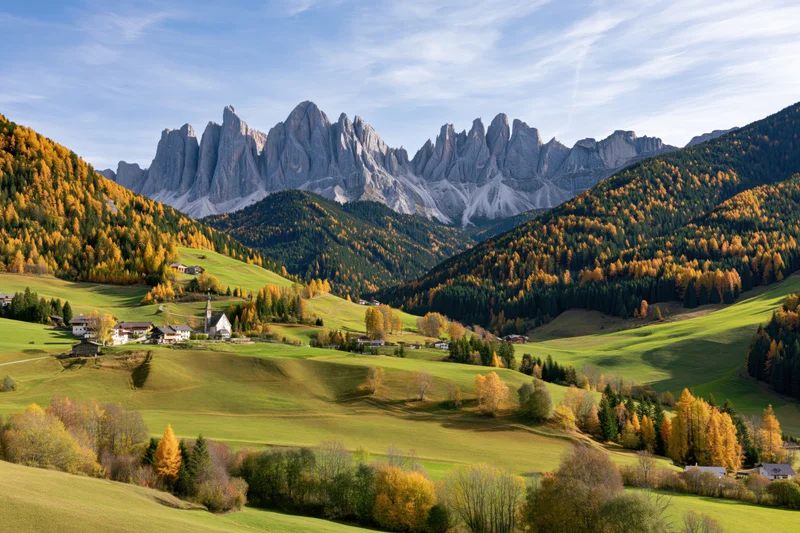 Autumnal valley with colorful trees and village nestled in the dolomites mountains