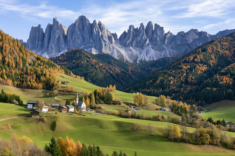 Alpine valley with autumn foliage and village nestled among mountains in val di funes, italy