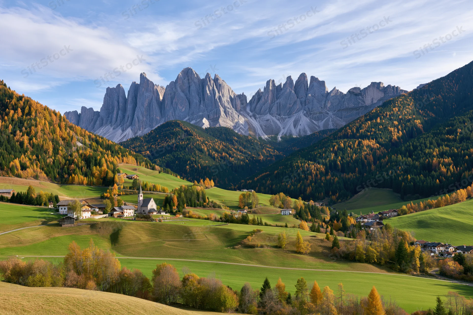 Alpine valley with village and church nestled among green hills and autumn trees under rocky dolomite peaks