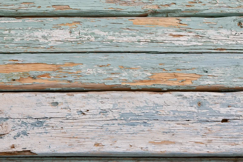 Horizontal weathered wooden planks with peeling blue and white paint forming a textured surface