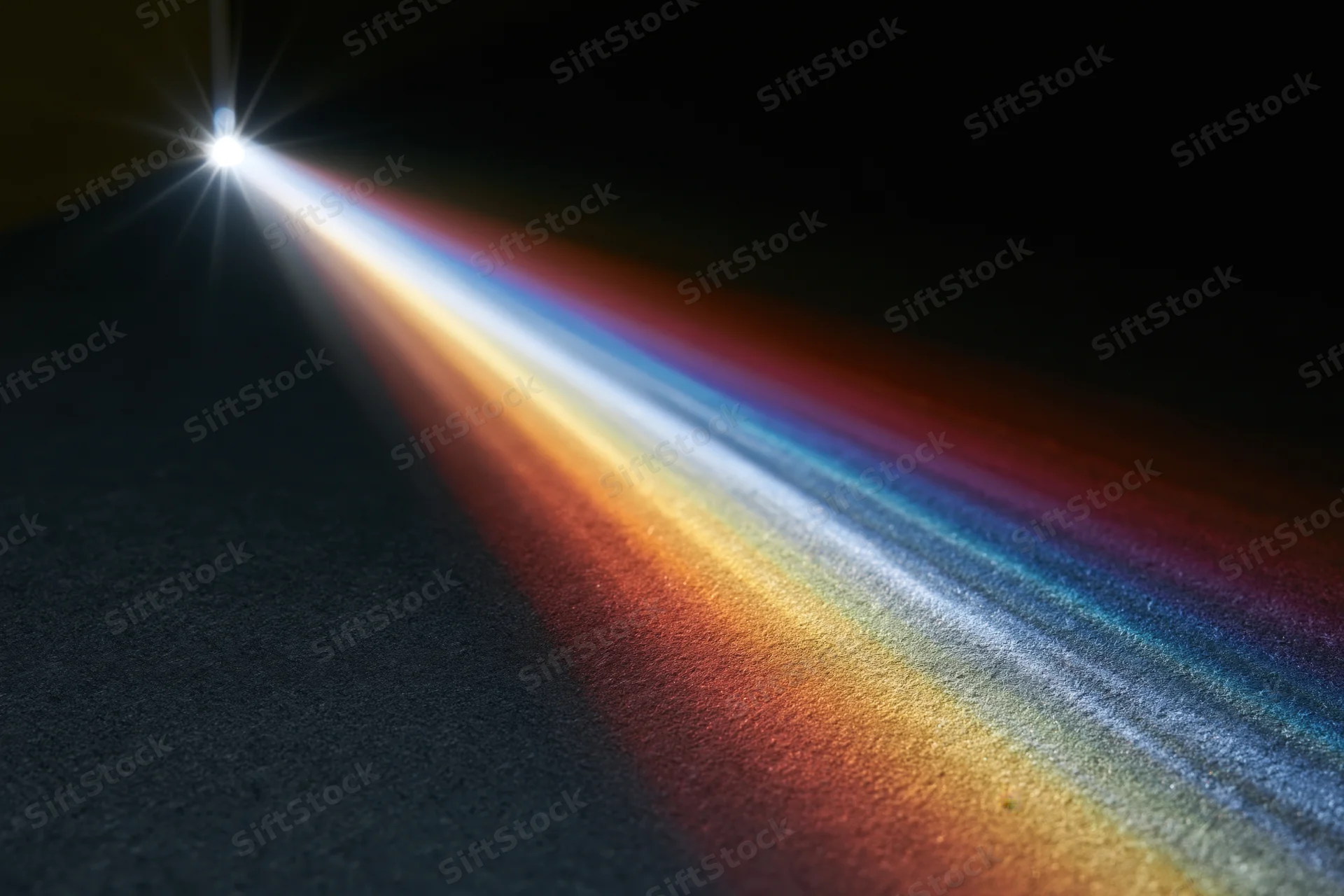 White light refracting through a glass prism edge casting a colorful spectrum on a dark surface
