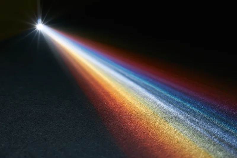 White light refracting through a glass prism edge casting a colorful spectrum on a dark surface