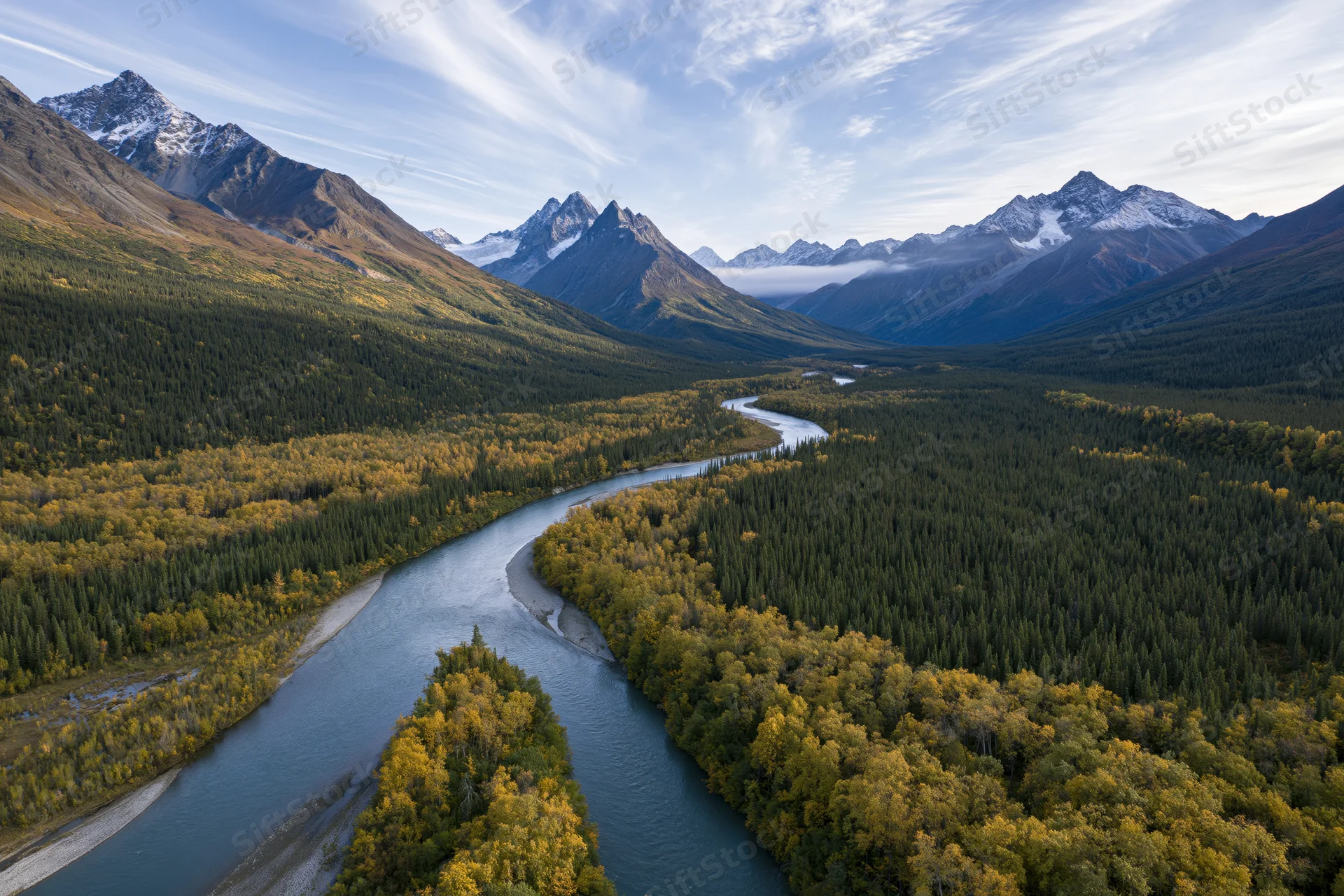 Winding river cutting through alpine valley surrounded by snow-capped mountains and autumn forest