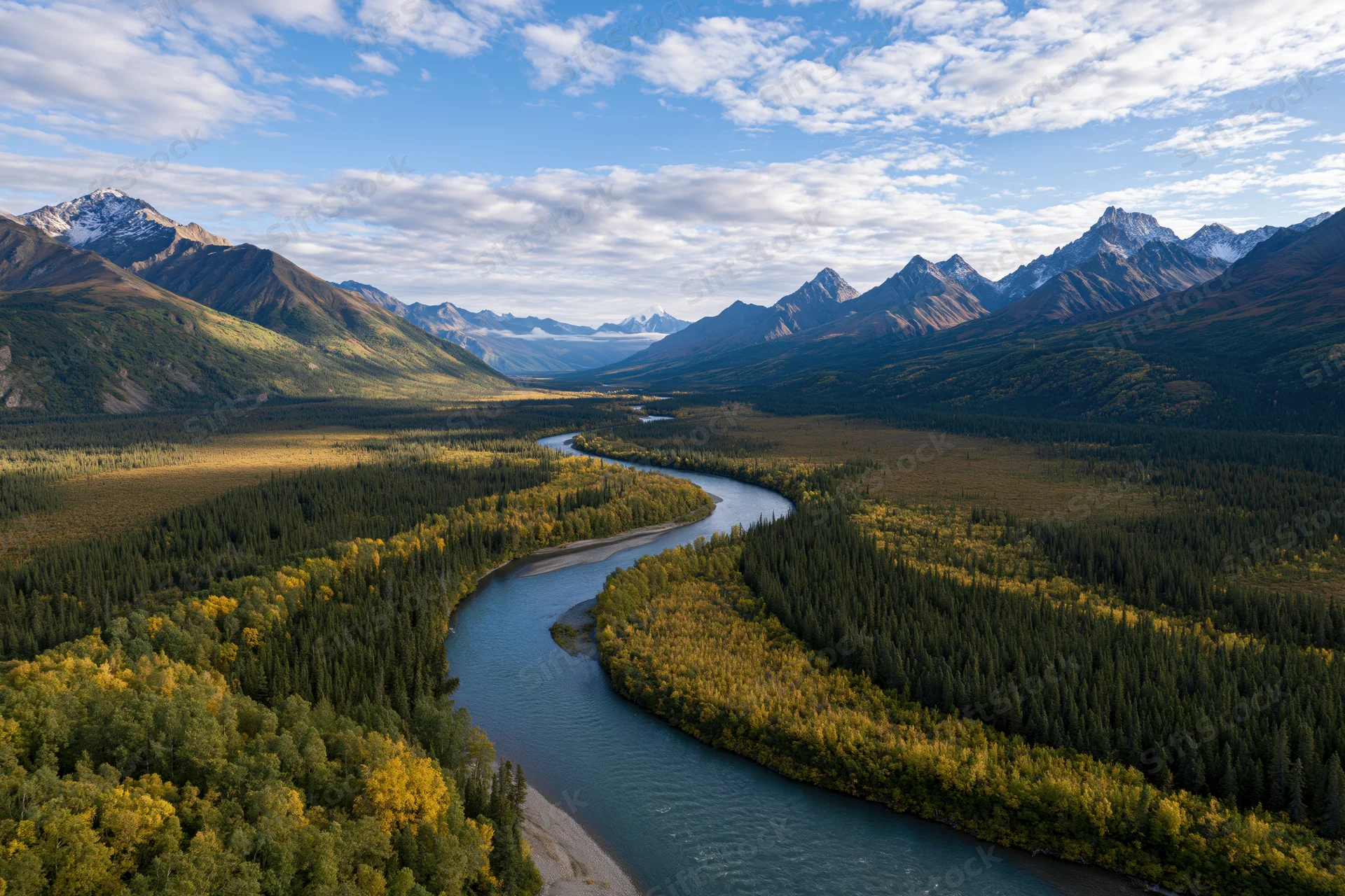 Winding river cutting through alpine valley surrounded by snow-capped mountains and autumn forest
