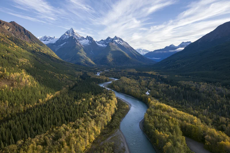 Winding river through alpine valley surrounded by snow-capped mountains and autumn forest