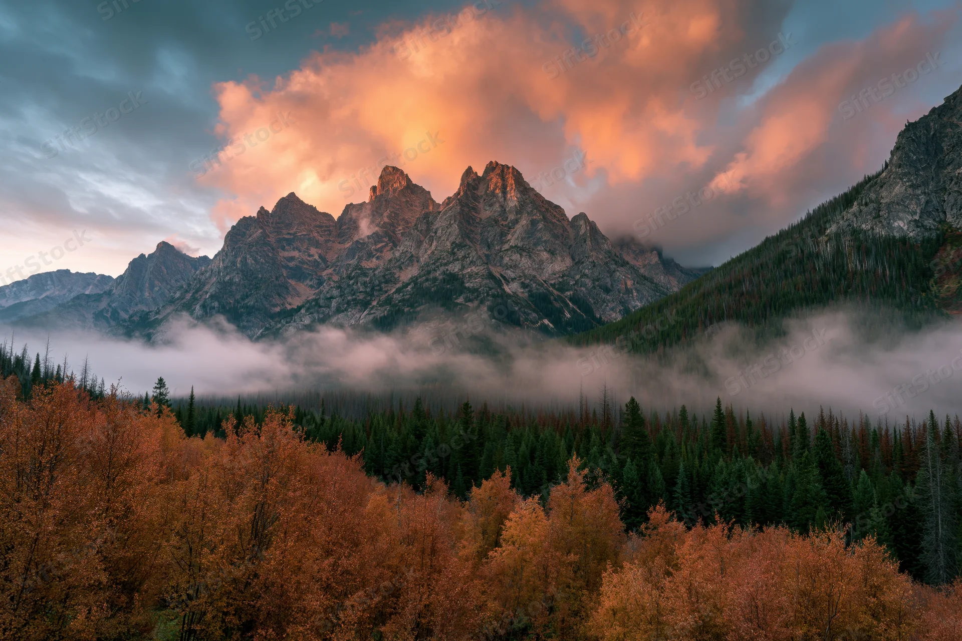 Jagged rocky mountain peaks rising above misty valley with autumn aspen and evergreen forest at sunrise