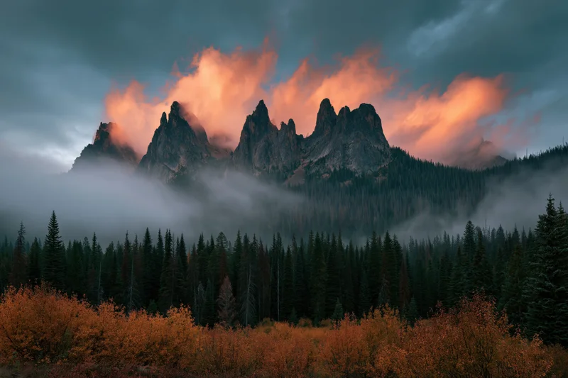 Jagged mountain peaks rising above foggy forest with autumn foliage in foreground