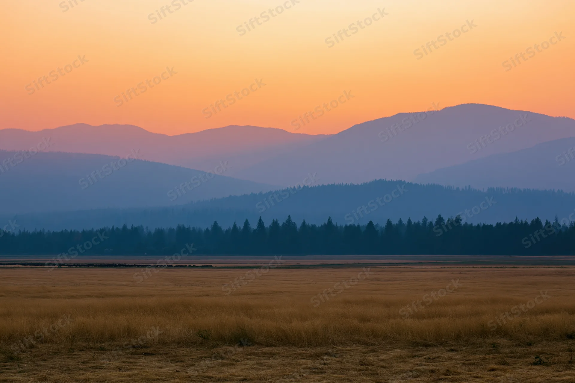 Flat agricultural fields stretching to distant mountains under a sunset sky