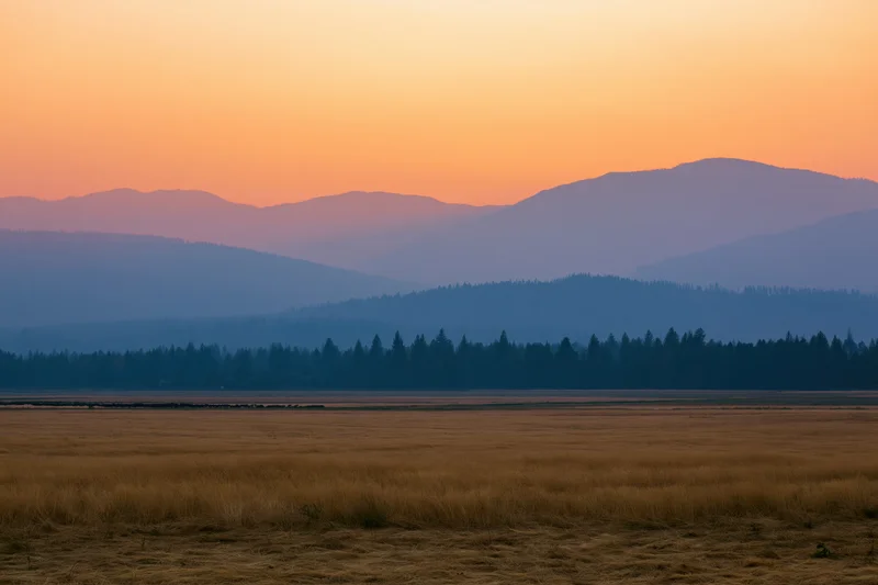 Flat agricultural fields stretching to distant mountains under a sunset sky