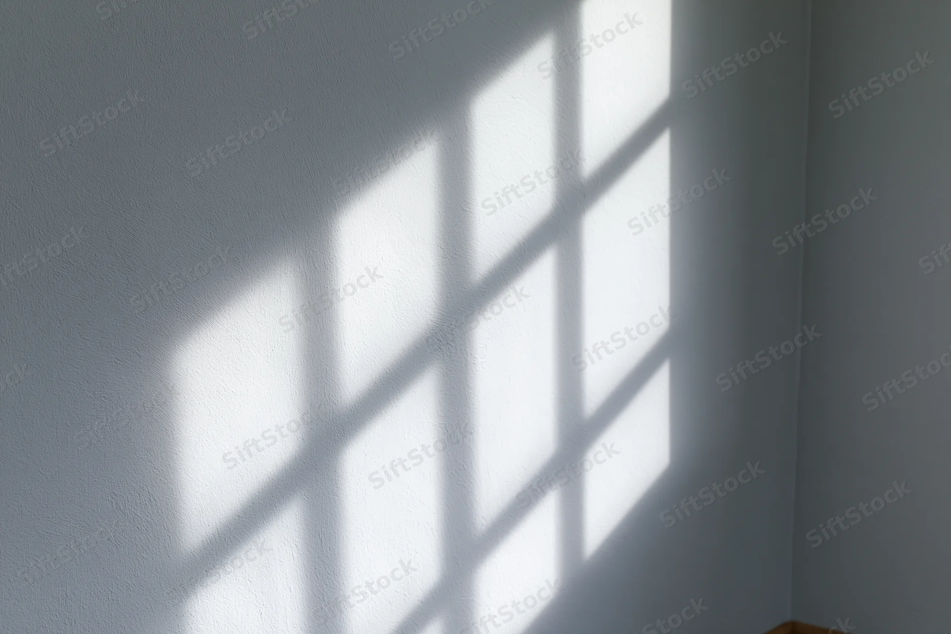 Diagonal window grid shadow cast across plain light gray wall in interior space