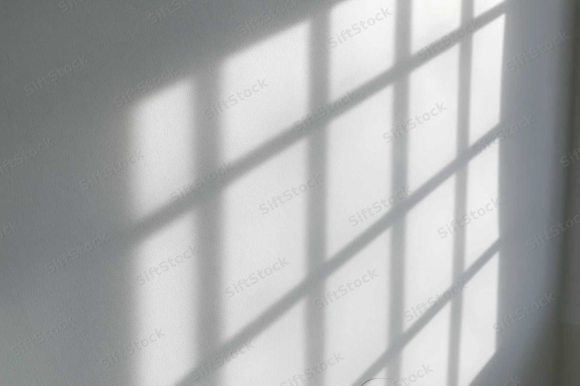 Diagonal window grid shadow cast across a plain white wall in an interior space