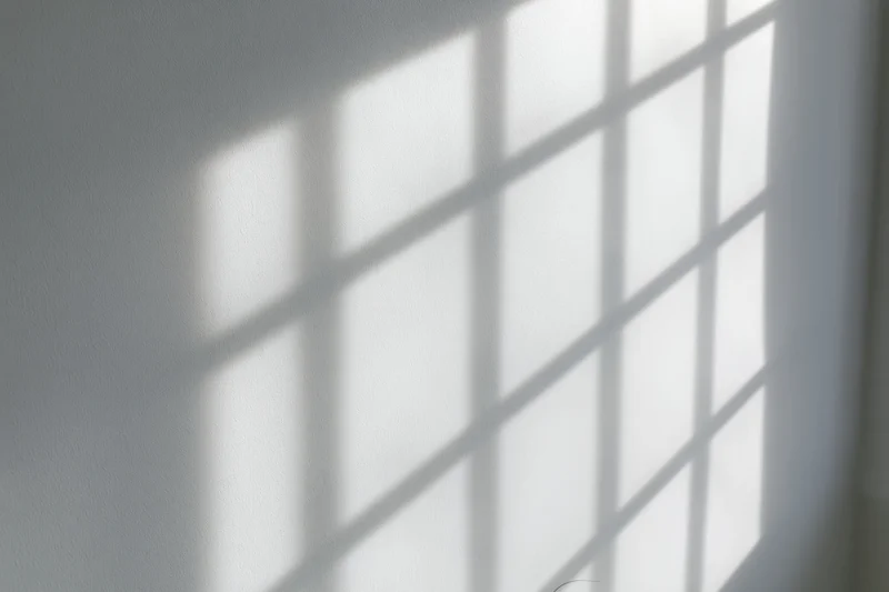 Diagonal window grid shadow cast across a plain white wall in an interior space