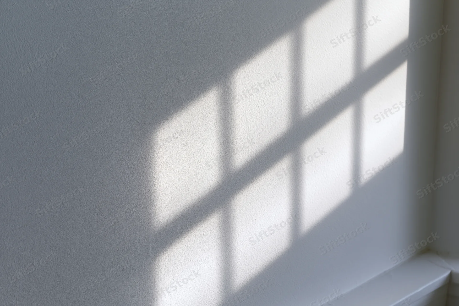 Diagonal window grid shadow cast across white interior wall in corner