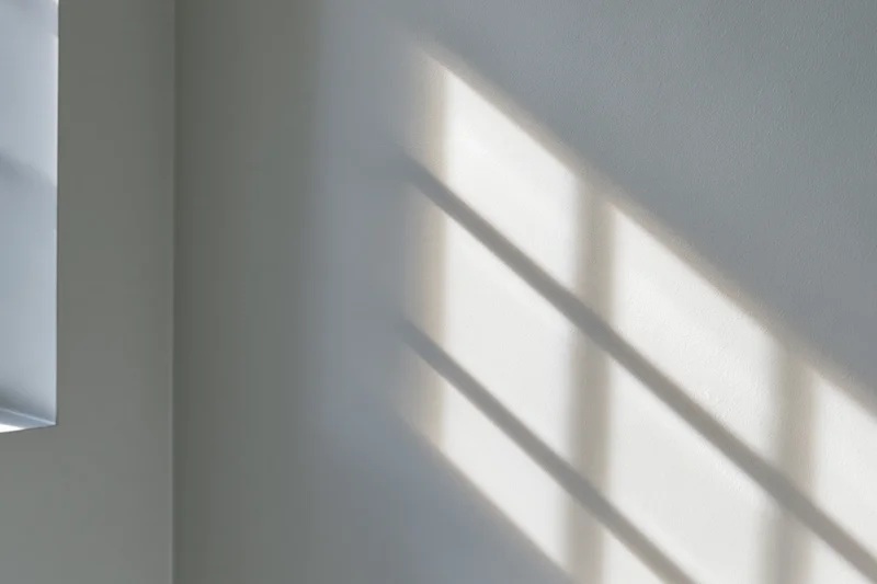 Diagonal window grid shadow cast across white-grey interior wall