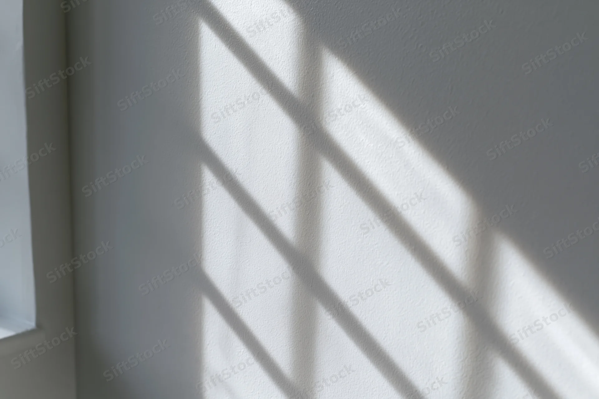 Diagonal window grid shadow cast across white-gray interior wall