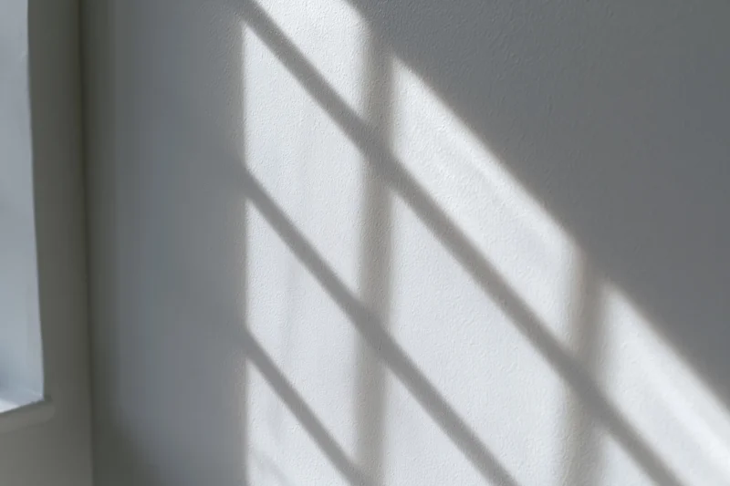 Diagonal window grid shadow cast across white-gray interior wall
