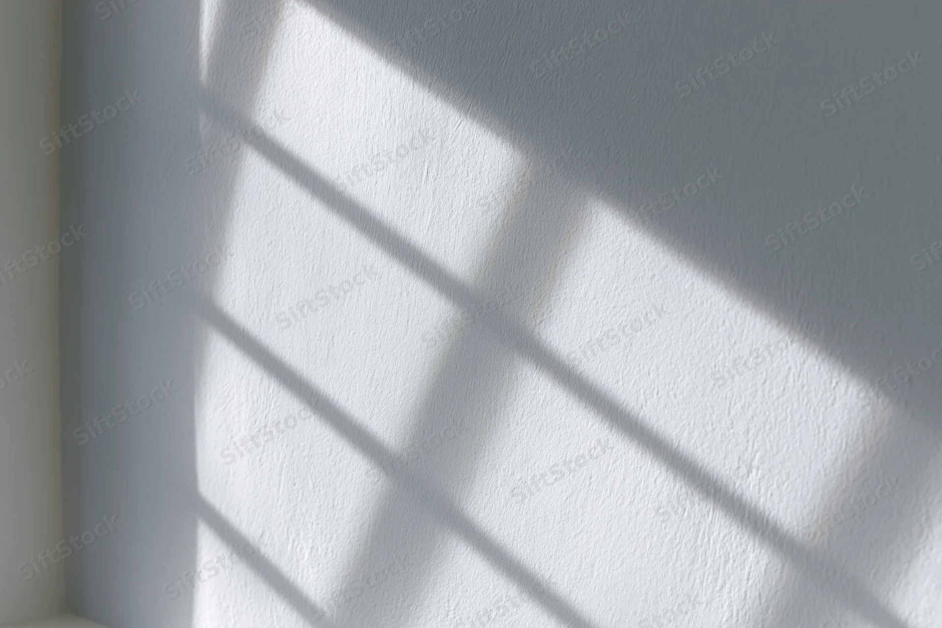 Diagonal window grid shadow cast across white textured wall in interior corner