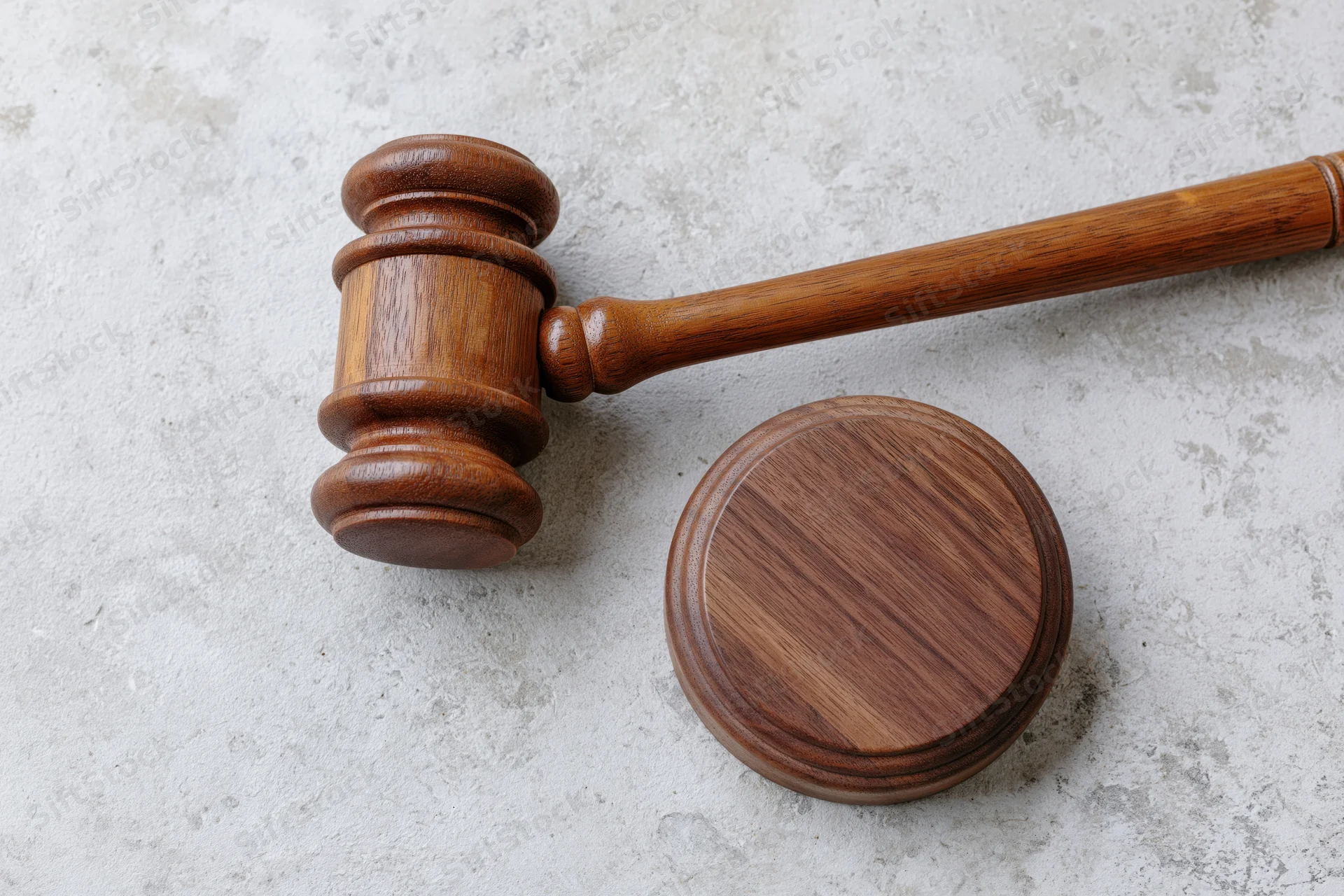 Wooden judge's gavel resting beside its round sound block on a textured concrete surface