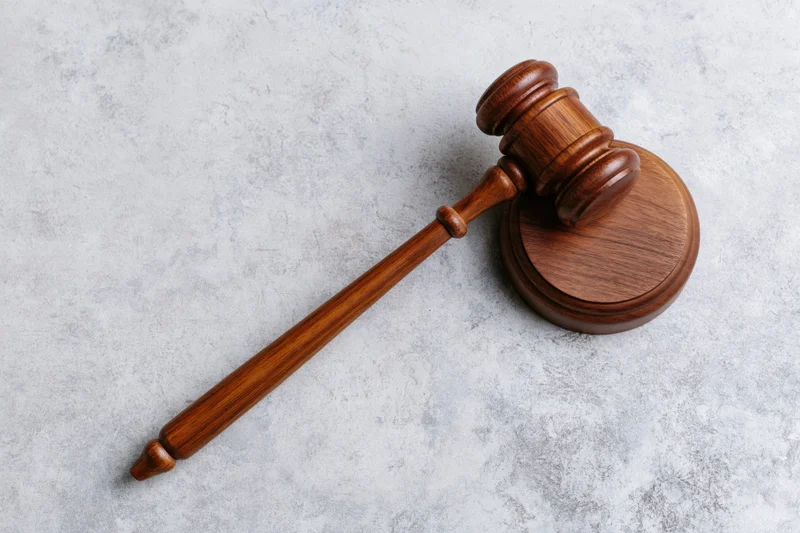 Wooden judge's gavel resting beside its round sound block on a textured gray surface