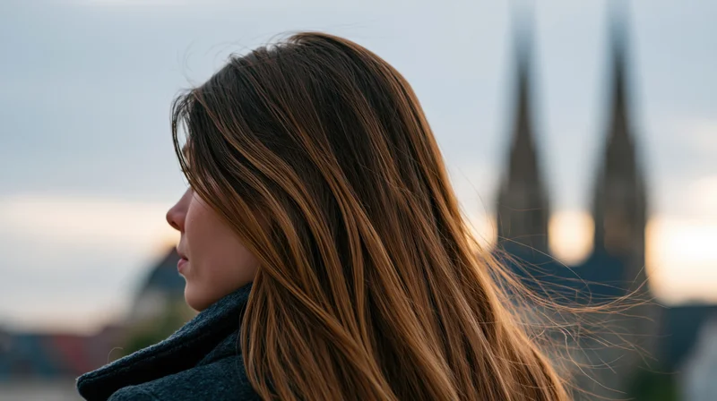 Young woman in profile with long brown hair blowing in the wind, facing city skyline at dusk