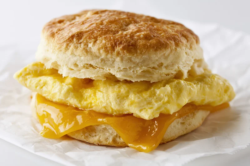 Southern-style buttermilk biscuit breakfast sandwich with scrambled egg and melted cheese on white paper