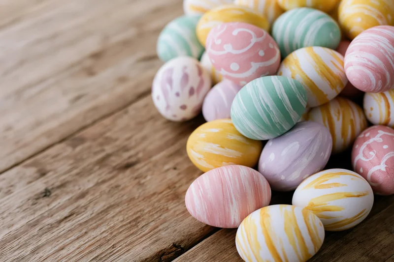 Hand-painted easter eggs piled on a rustic wooden surface with copyspace on the left