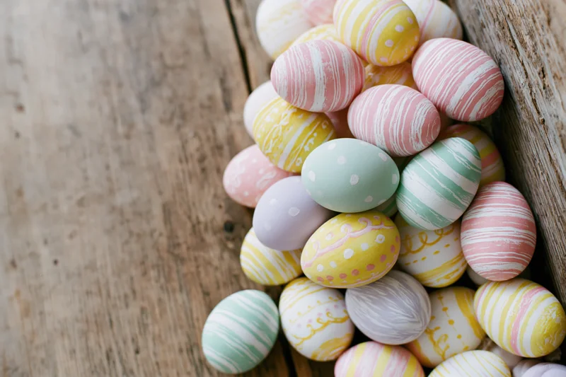 Hand-painted easter eggs piled along wooden surface with copyspace on left