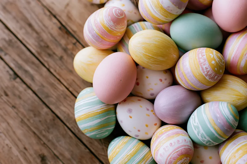 Hand-painted easter eggs piled on a wooden surface with copyspace on the left
