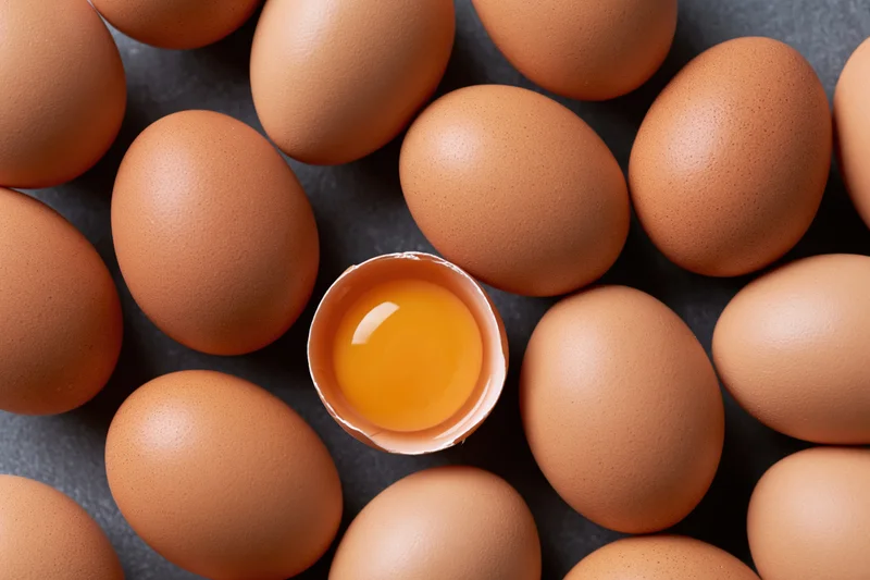 Brown chicken eggs arranged on dark surface with one cracked open revealing yolk