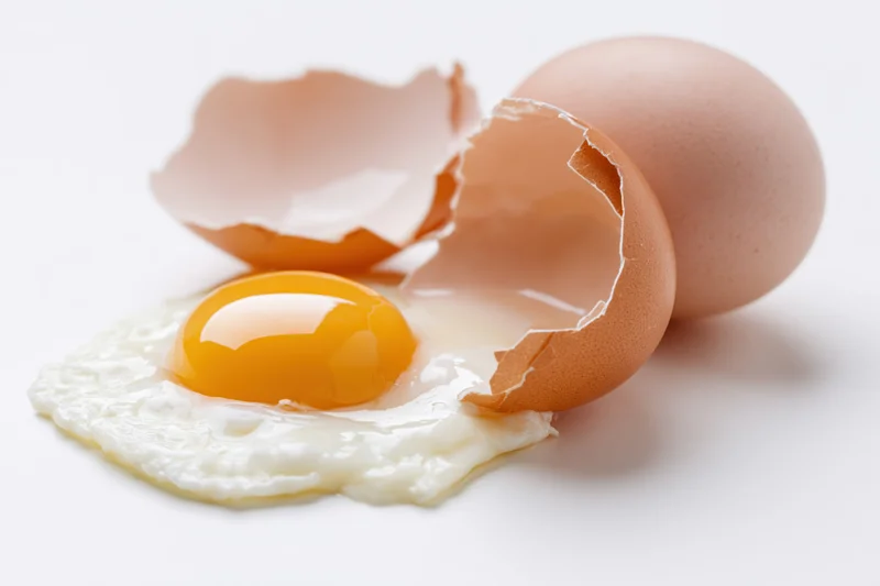 Cracked brown egg with intact yolk and shell fragments on white surface