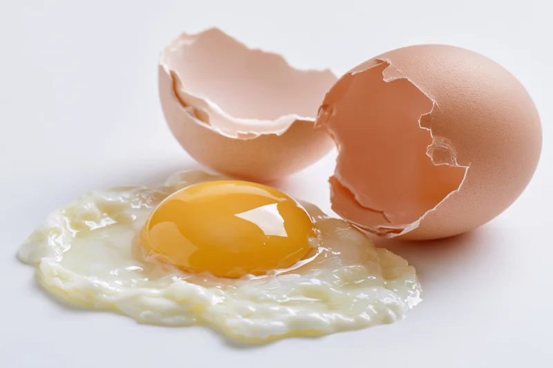 Cracked brown egg with intact yolk and shell halves on white surface