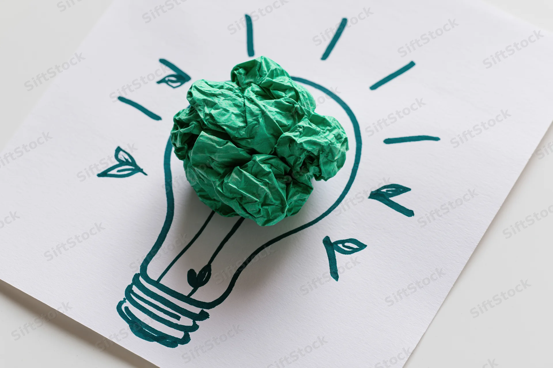 Crumpled green paper ball placed on a hand-drawn lightbulb sketch on white paper