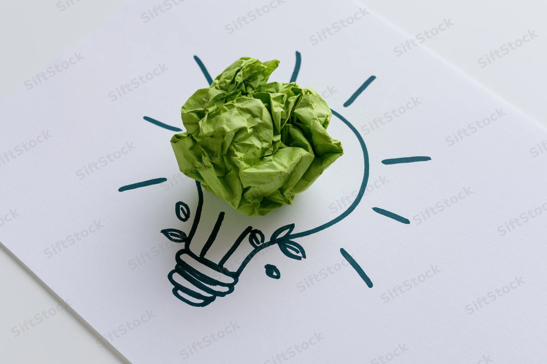 Crumpled green paper ball placed on a hand-drawn lightbulb sketch on white card