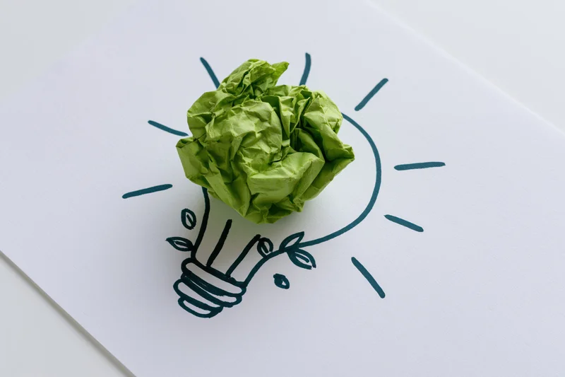 Crumpled green paper ball placed on a hand-drawn lightbulb sketch on white card
