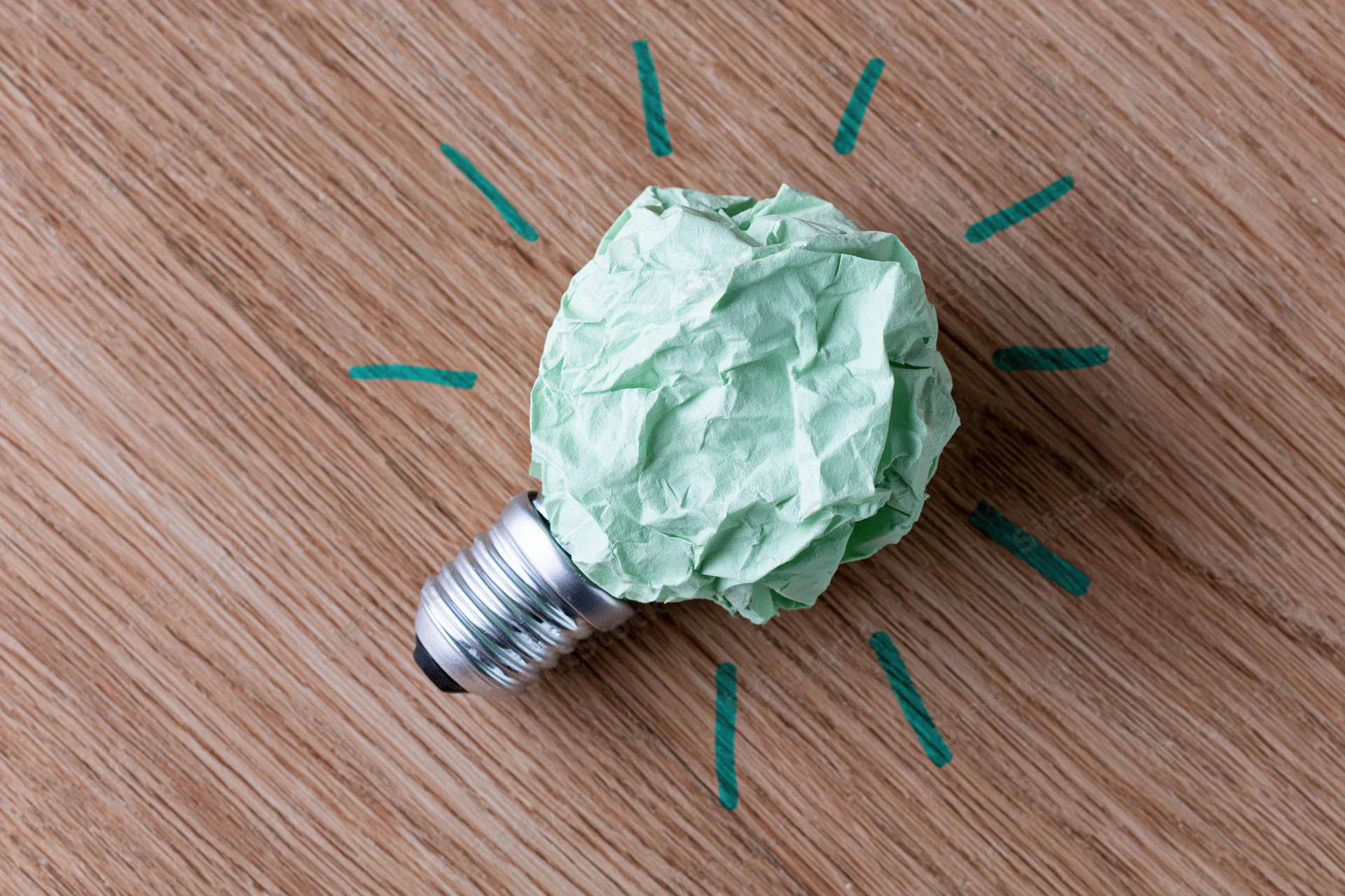 Crumpled green paper ball on silver lightbulb base resting on wooden surface