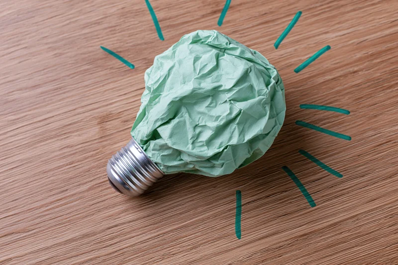 Crumpled green paper ball resting on silver light bulb base on wooden surface