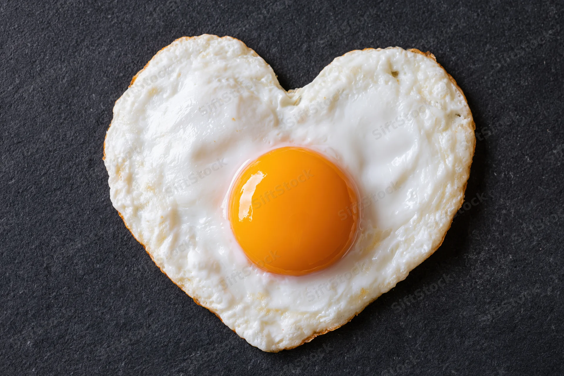 Fried egg cooked in heart shape sunny side up on dark surface