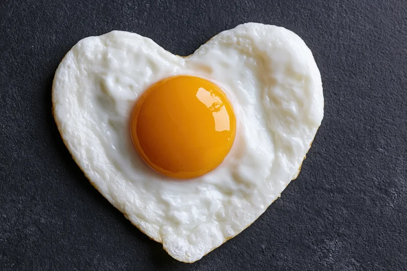 Fried egg cooked in heart shape sunny side up on dark surface