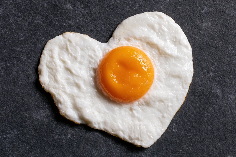 Fried egg cooked into heart shape sunny side up on dark slate surface