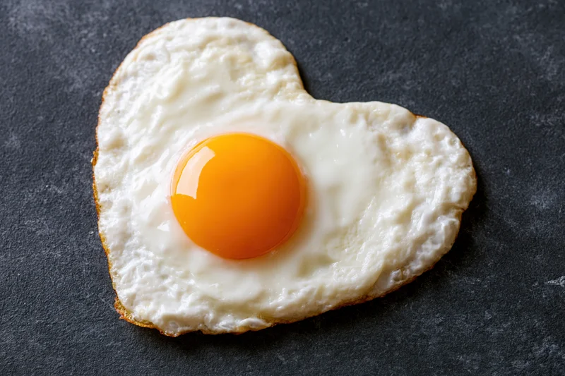 Fried egg cooked into heart shape sunny side up on dark surface