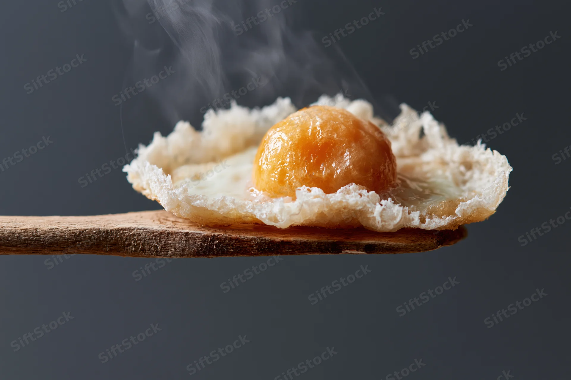 Fried sunny-side-up egg with runny yolk and steam resting on a worn wooden spatula