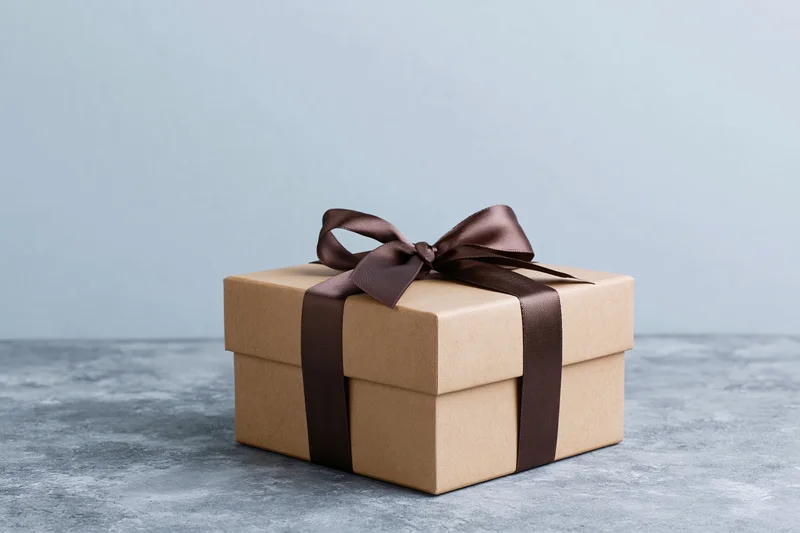 Kraft brown gift box tied with dark chocolate ribbon on gray concrete surface