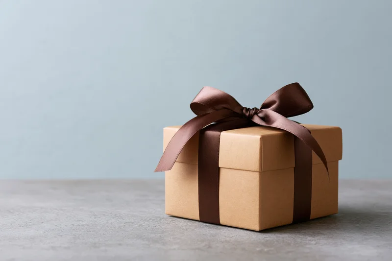 Kraft cardboard gift box tied with dark chocolate satin ribbon on gray concrete surface