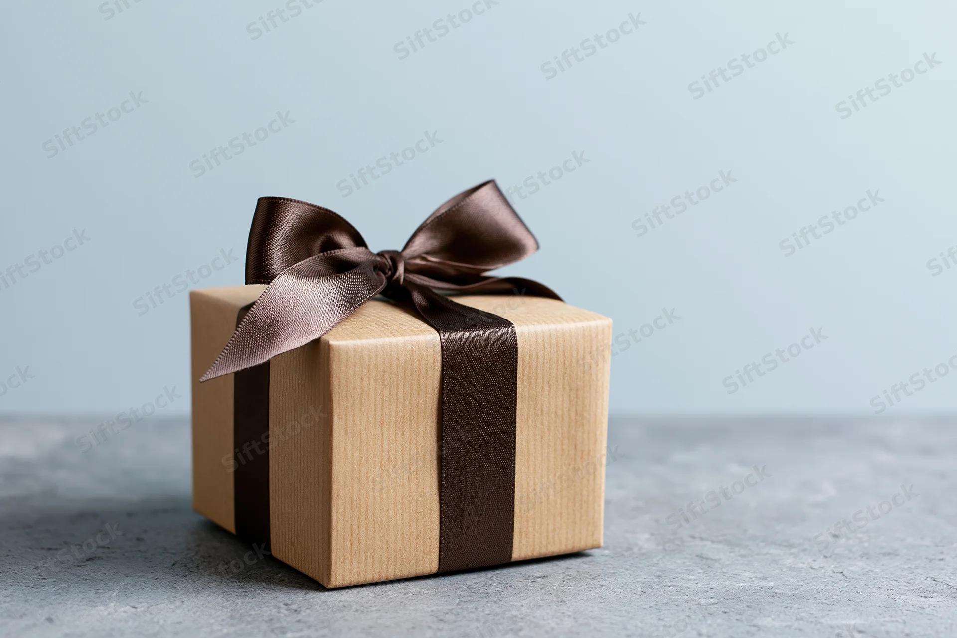 Kraft brown gift box tied with dark chocolate ribbon on gray surface