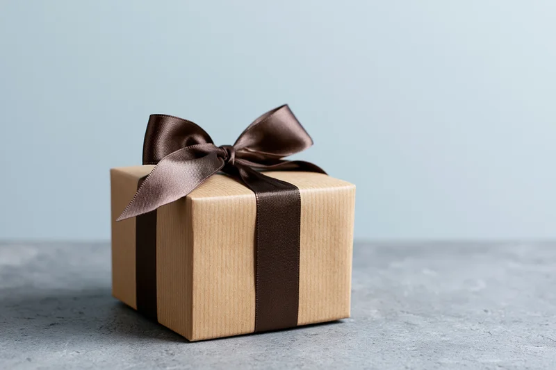 Kraft brown gift box tied with dark chocolate ribbon on gray surface