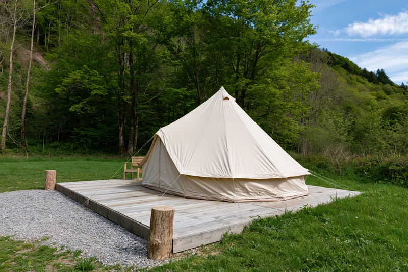 Large canvas bell tent on wooden deck surrounded by forest and greenery