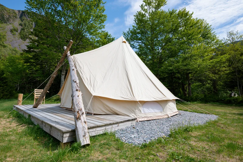 Large canvas bell tent on wooden deck surrounded by trees and mountains