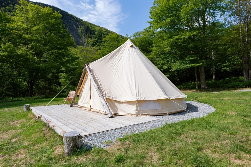 Large canvas bell tent on wooden deck surrounded by green forest and mountains during daytime